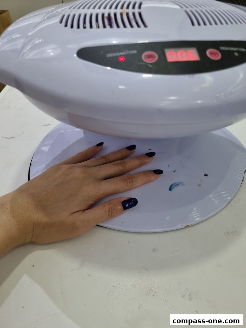 A hand with dark blue nails is placed under a nail dryer.