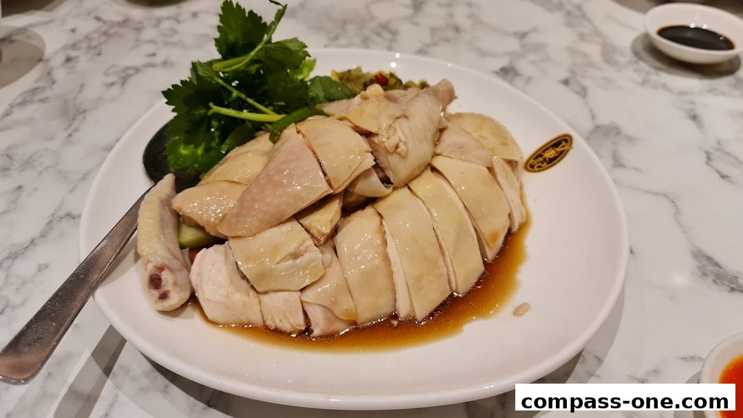 A plate of sliced poached chicken with herbs and dipping sauce.
