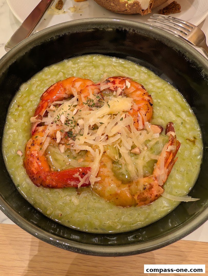 A close-up of creamy green risotto topped with grilled prawns and grated cheese.
