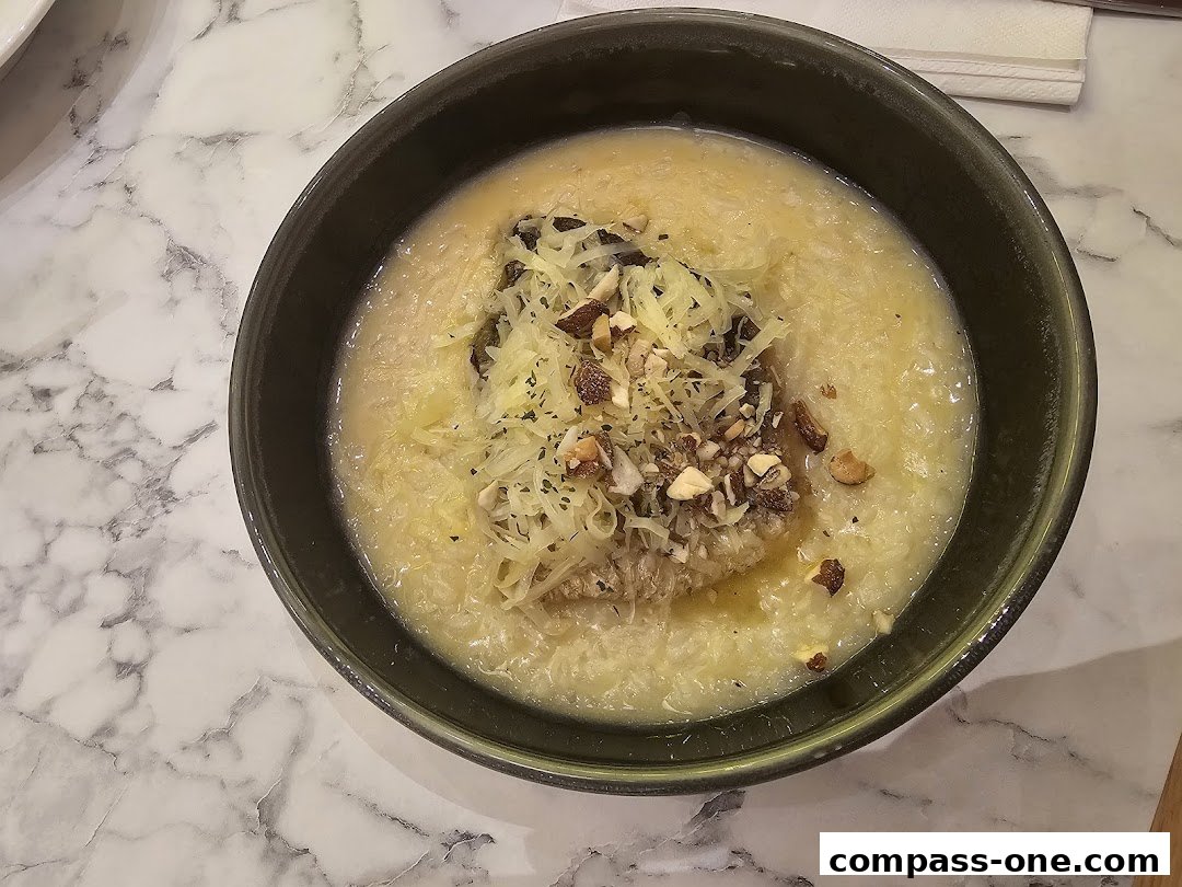 A close-up shot of a bowl of soup topped with cheese, nuts, and herbs.