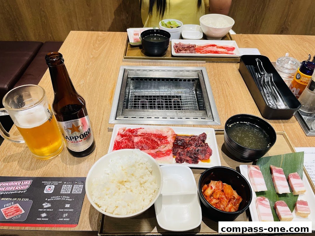 A table set for a Yakiniku meal with grilled meats, rice, soup, kimchi, and beer.