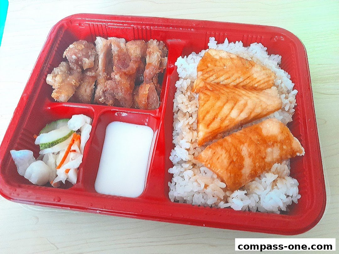 A bento box with fried chicken, grilled salmon, rice, and pickled vegetables.