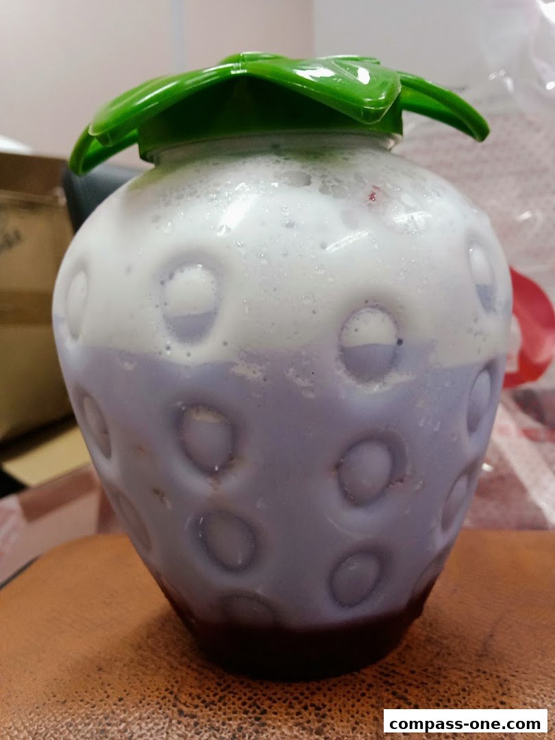 A close-up of a strawberry-shaped cup filled with a layered purple and white beverage.