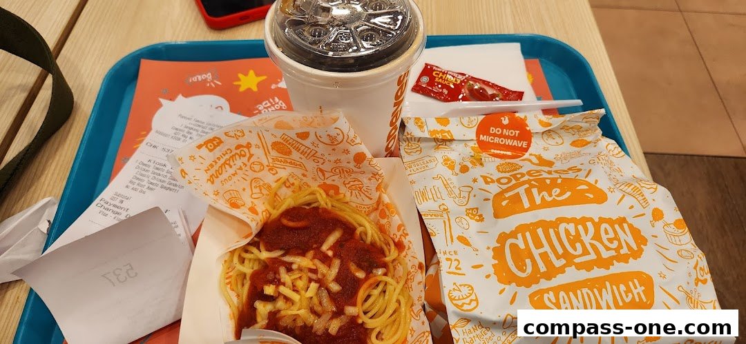 A tray of Popeyes food including a chicken sandwich, spaghetti, and a drink.