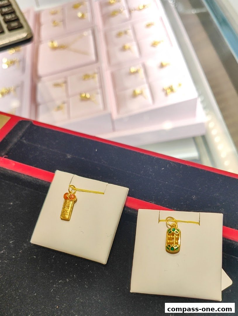 Close-up of two gold pendants displayed on white cards, with a blurred background of jewelry.