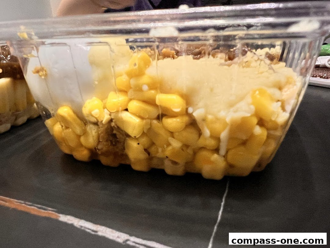 A clear plastic container filled with corn, mashed potatoes, and meat.