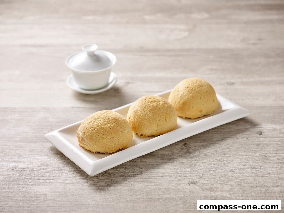 Three golden-brown baked buns served on a white rectangular plate with a tea cup in the background.