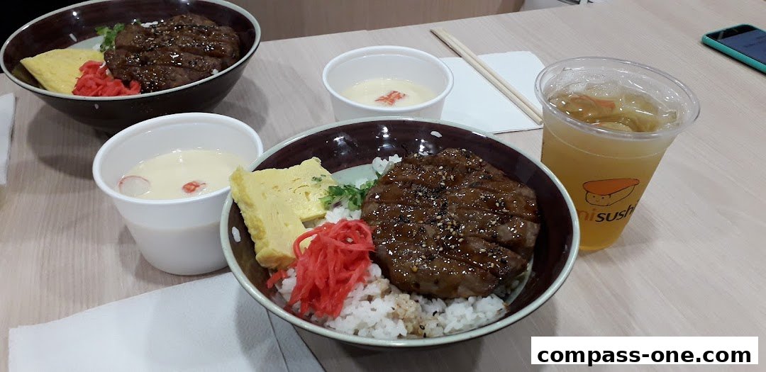 Two bowls of donburi with grilled meat, tamagoyaki, and pickled ginger, plus a drink.
