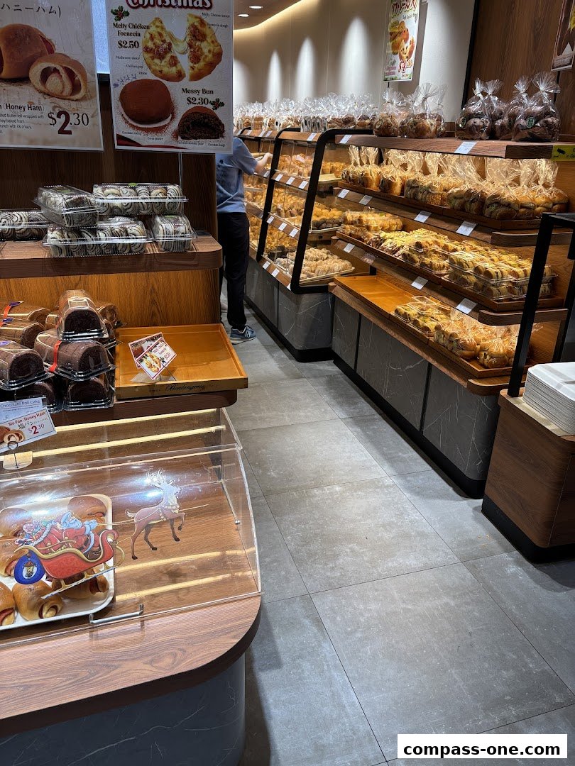 A bakery display filled with various pastries and breads, with a staff member arranging items.