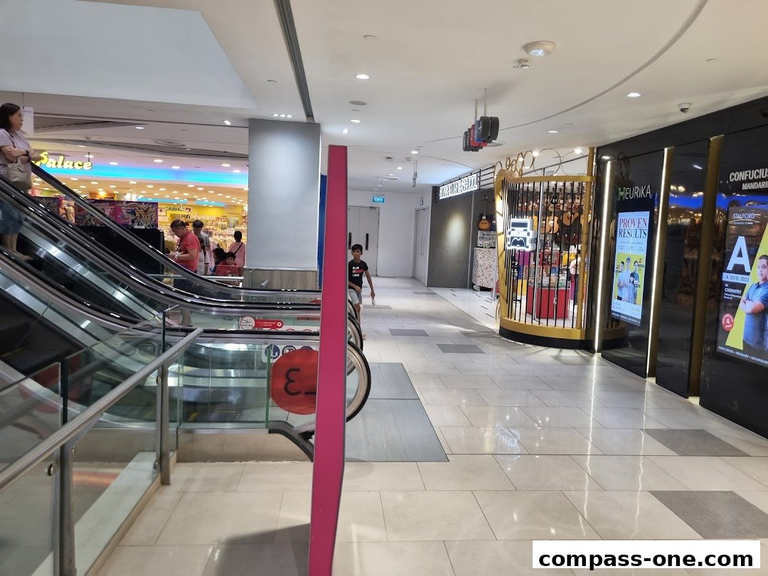 A shopping mall corridor with escalators, shops, and people walking.