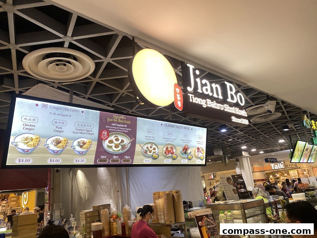 A brightly lit menu board for Jian Bo, showcasing congee and shui kueh dishes with prices.