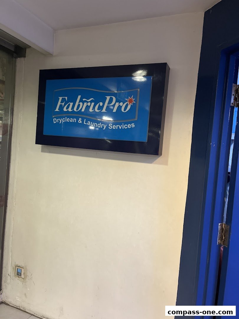 A sign for FabricPro Dryclean & Laundry Services is mounted on a wall next to a blue door.