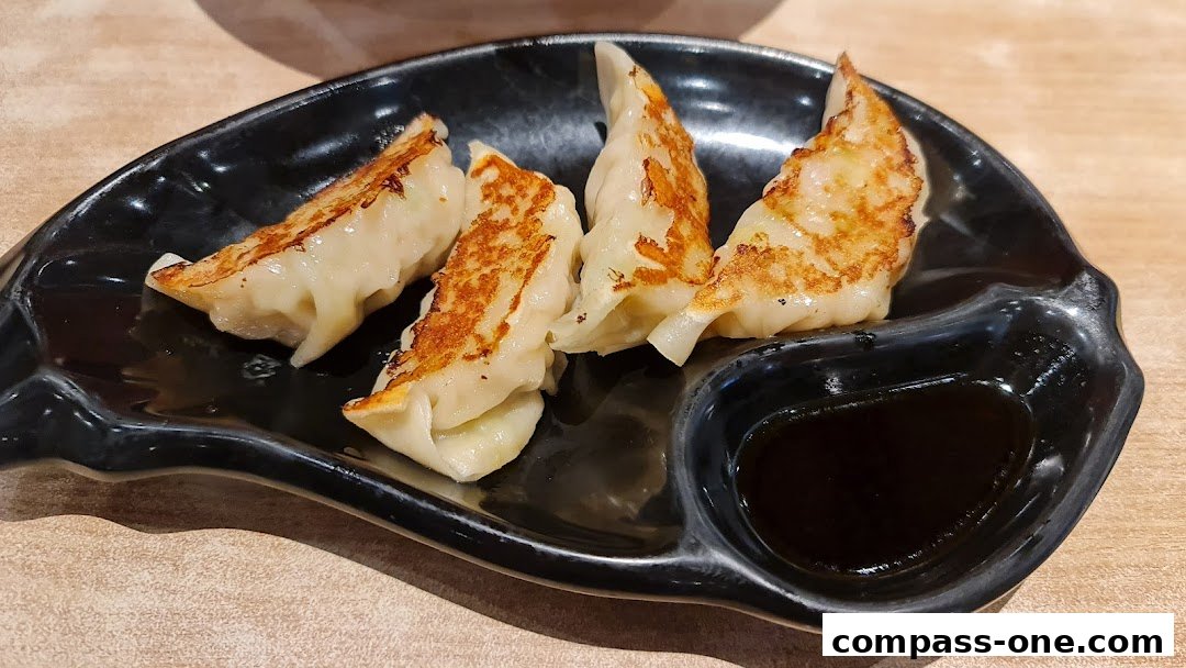 A plate of pan-fried gyoza dumplings with a side of dipping sauce.