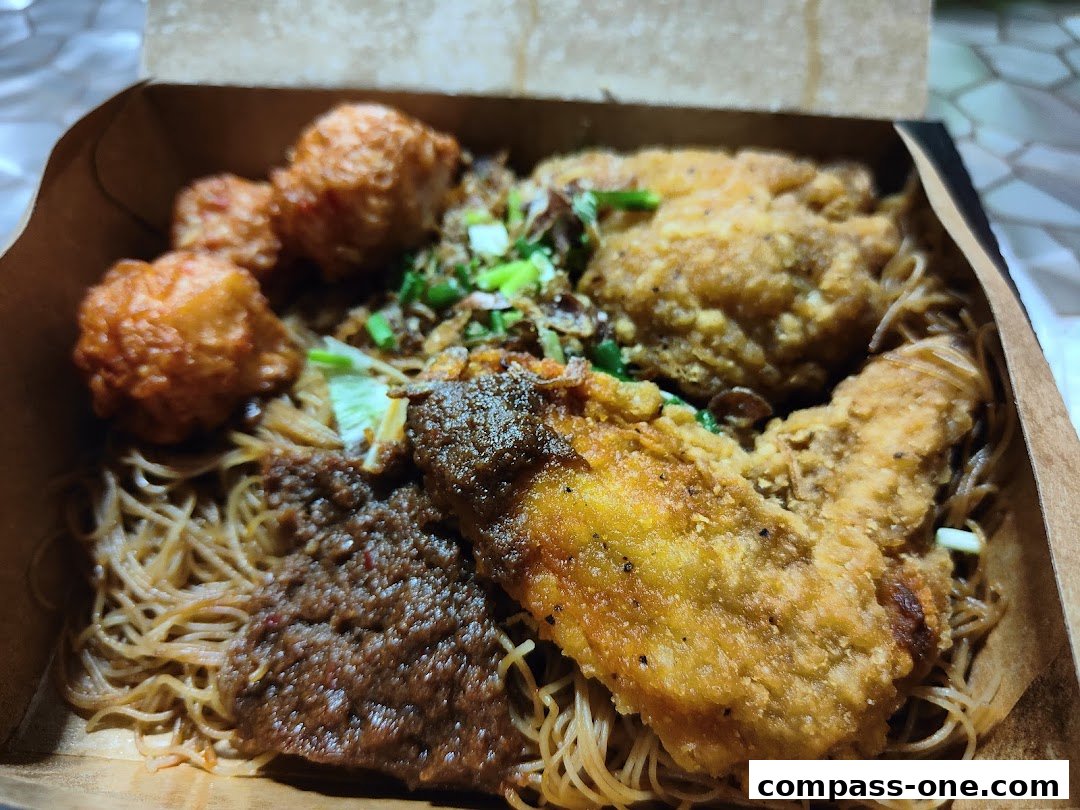 A close-up of a takeaway box filled with noodles, fried chicken, and meatballs.