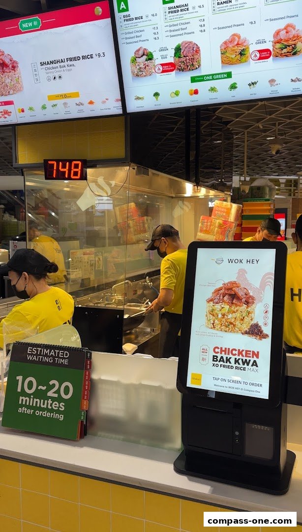 Wok Hey staff preparing food behind a counter with digital menus and a waiting time display.