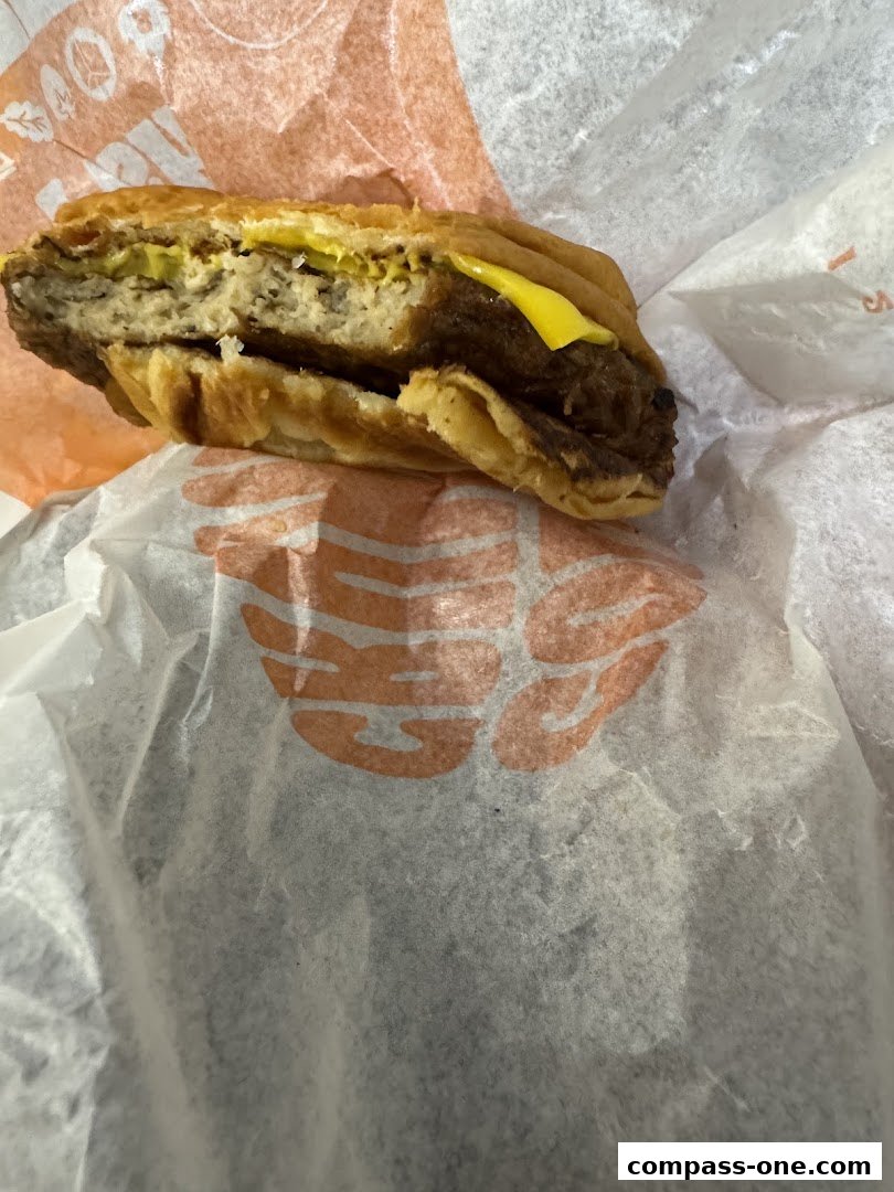 A close-up shot of a halved burger with cheese and pickles, wrapped in Burger King branded paper.
