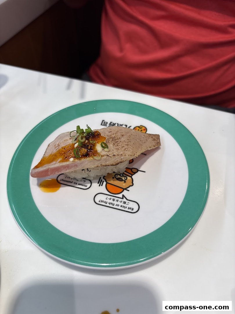 A plate of sushi with a slice of seared tuna and toppings on a white table.