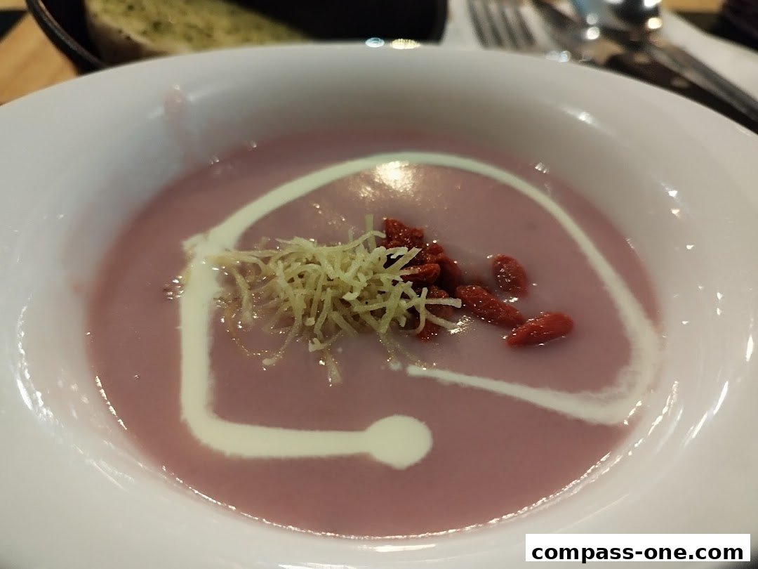 A close-up of a bowl of creamy purple soup topped with goji berries and shredded garnish.