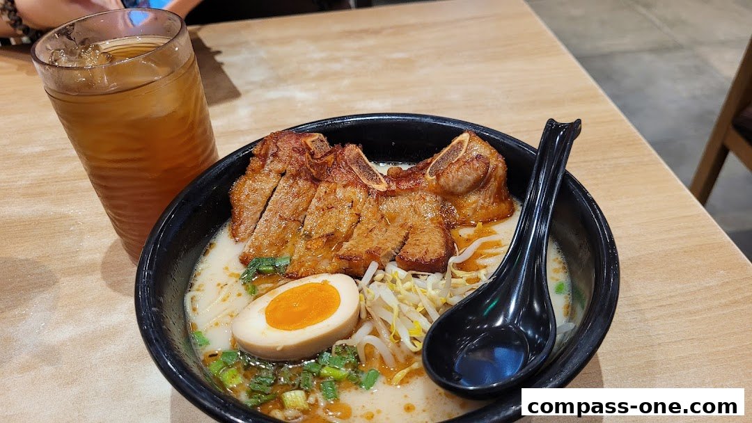 A bowl of Ajisen Ramen with pork ribs, egg, and bean sprouts, served with iced tea.