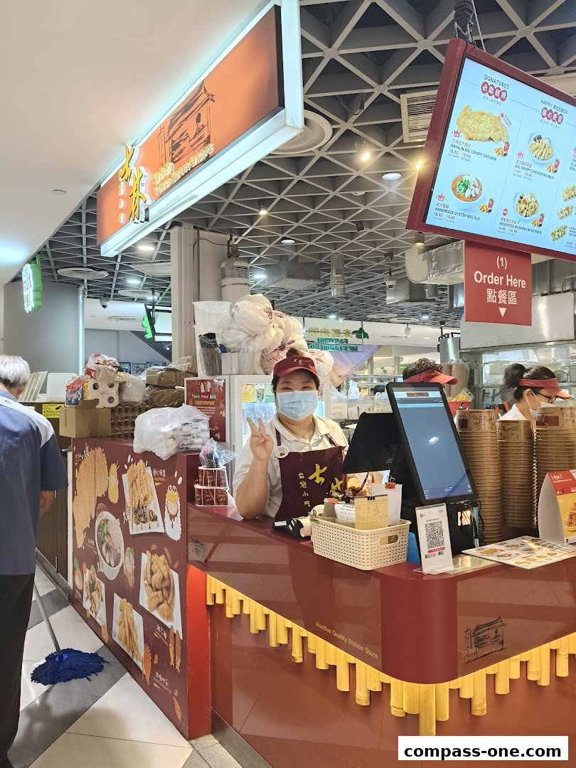 A Shihlin Taiwan Street Snacks stall with a staff member posing and a menu board above.