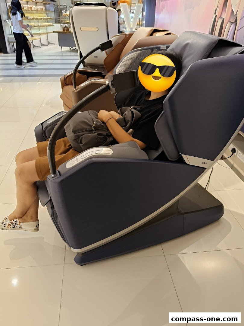 A person sits in a dark blue OSIM massage chair, with other chairs visible.