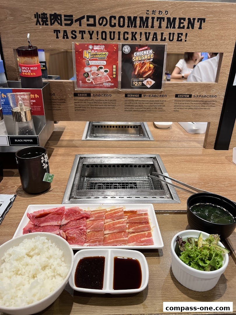 A table setting at Yakiniku Like with raw meat, rice, sauces, soup, salad, and a grill.