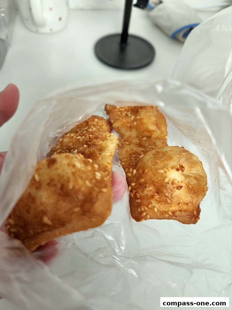 A hand holds a plastic bag filled with golden-brown, sesame-seed-covered fried dough pastries.