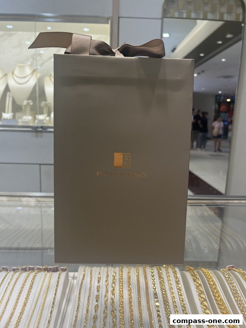 A gift bag with Poh Heng Jewellery logo sits above a display of gold necklaces.