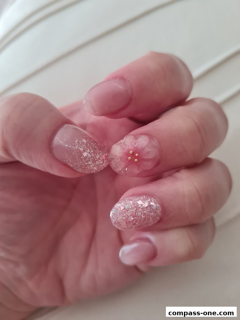 Close-up of a hand with beautifully decorated nails featuring glitter and a delicate floral design.