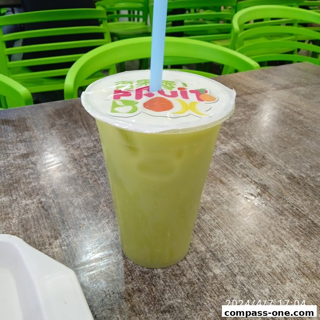 A tall cup of green juice with a blue straw and the Fruit Box logo on the lid.