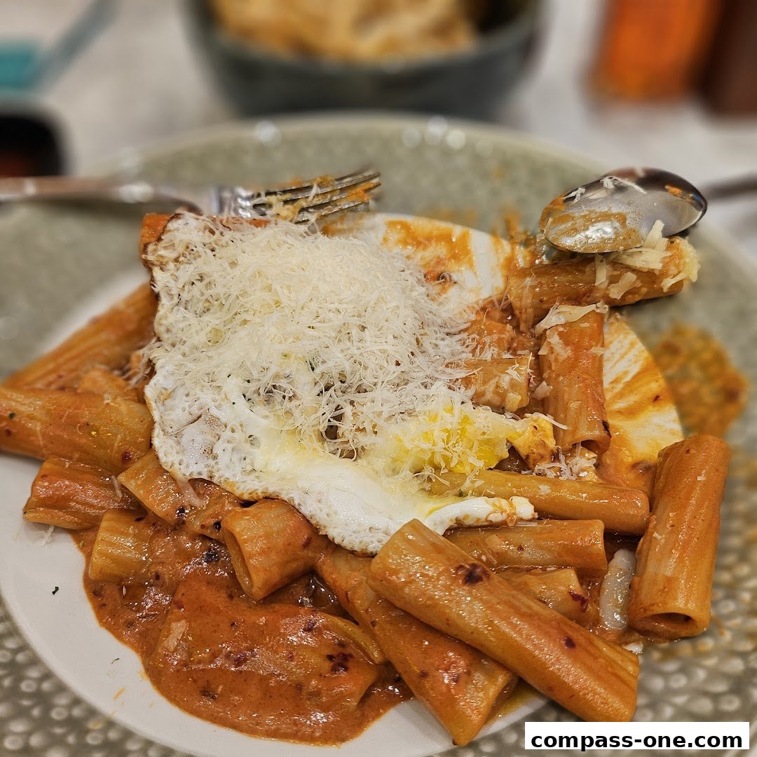 A close-up shot of rigatoni pasta with a creamy tomato sauce, topped with a fried egg and grated cheese.