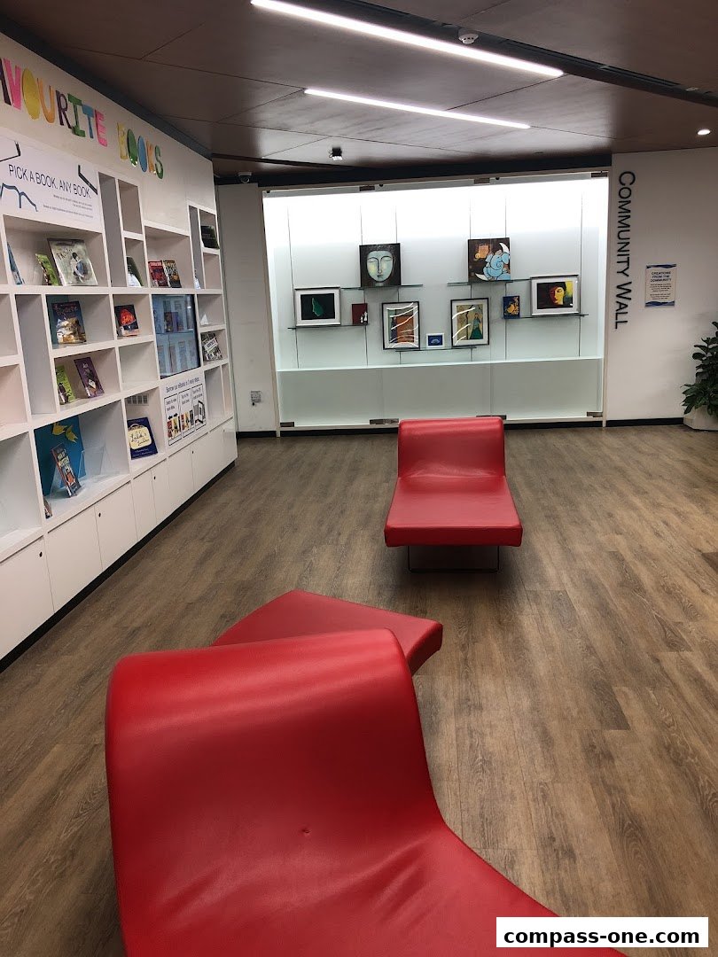 Interior of a library with bookshelves, art on display, and red lounge chairs.
