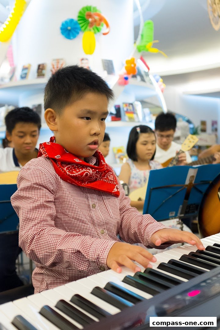 A young boy plays a keyboard while other students learn music in the background.