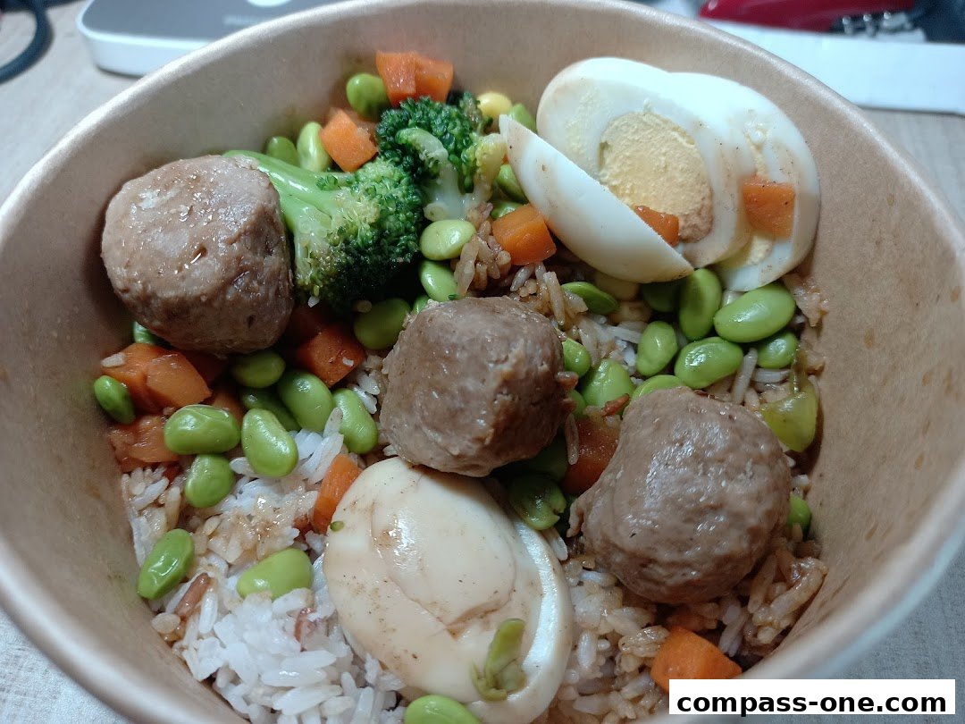A bowl of rice with meatballs, edamame, broccoli, carrots, and hard-boiled eggs.