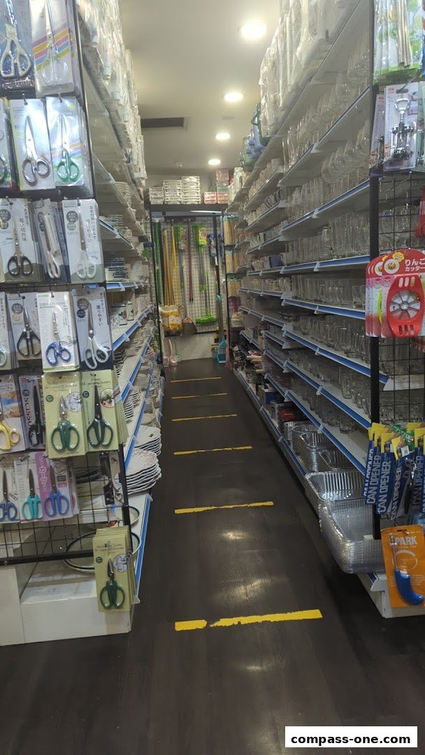Aisle view of a household goods store with shelves stocked with scissors, glassware, and kitchenware.