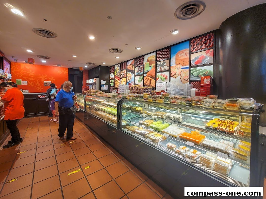 Customers queue inside a bakery displaying a wide variety of pastries and cakes.