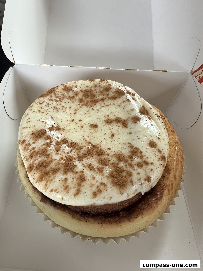 A close-up of a freshly baked cinnamon roll with cream cheese frosting and cinnamon dusting.
