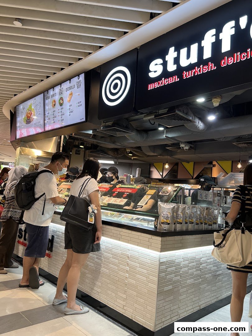 Customers ordering at a food stall with a menu board and display counter.