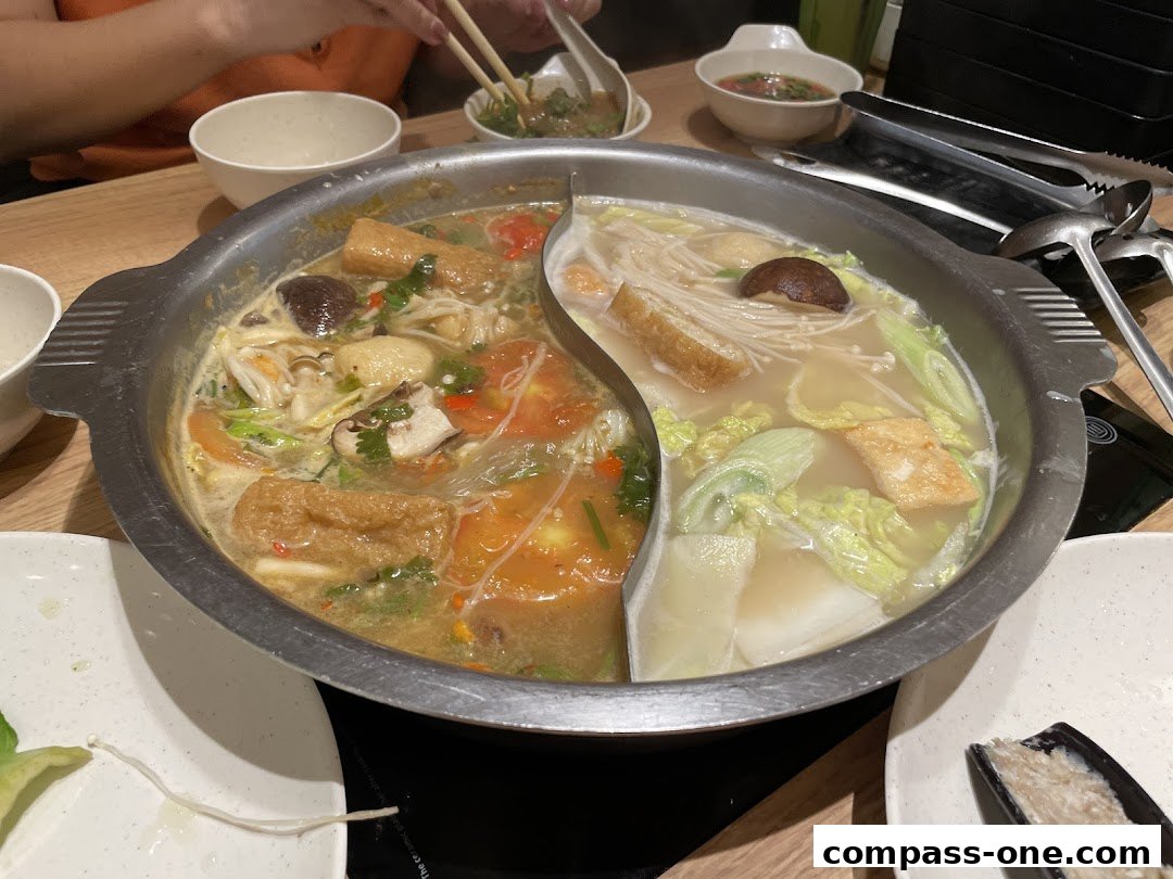A split pot of hot pot with various ingredients like tofu, mushrooms, and vegetables.