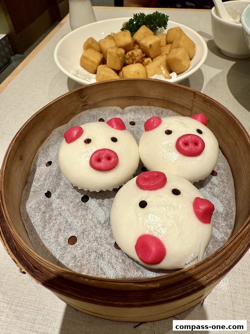 Three adorable pig-shaped steamed buns served in a bamboo steamer with a dish of fried tofu in the background.