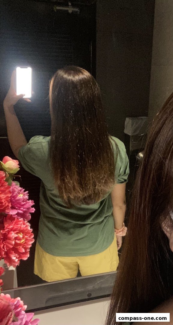 A person with long brown hair is taking a mirror selfie with a phone.