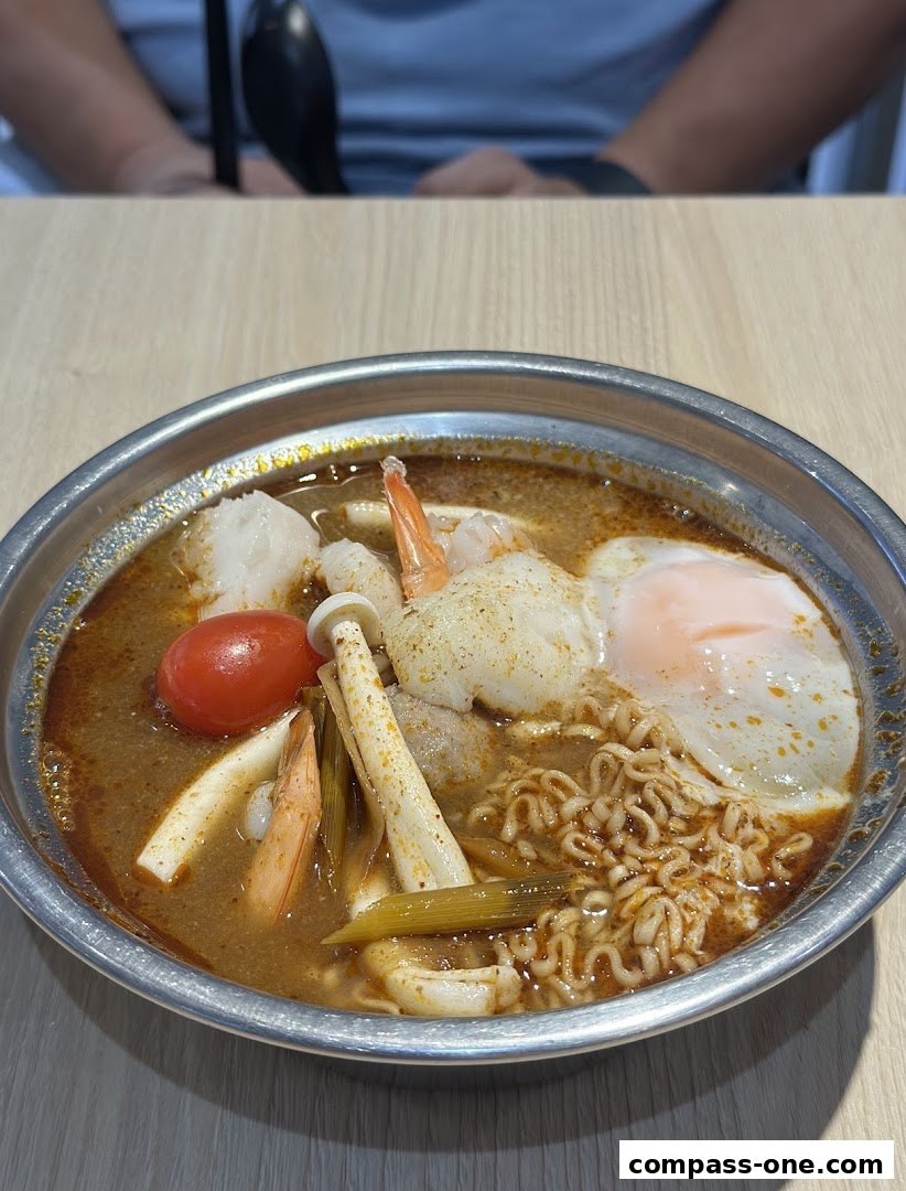 A close-up of a steaming bowl of noodles with shrimp, egg, and vegetables.