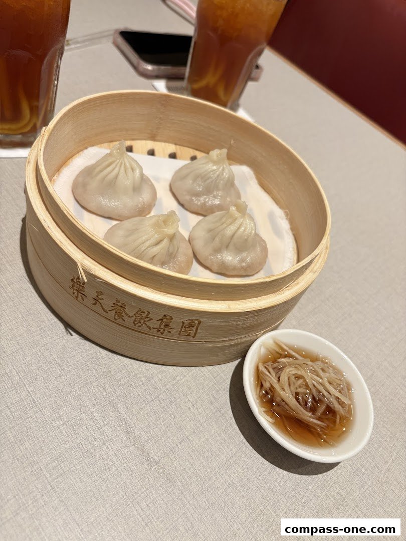 A close-up of Xiao Long Bao served in a bamboo steamer with dipping sauce and iced tea.