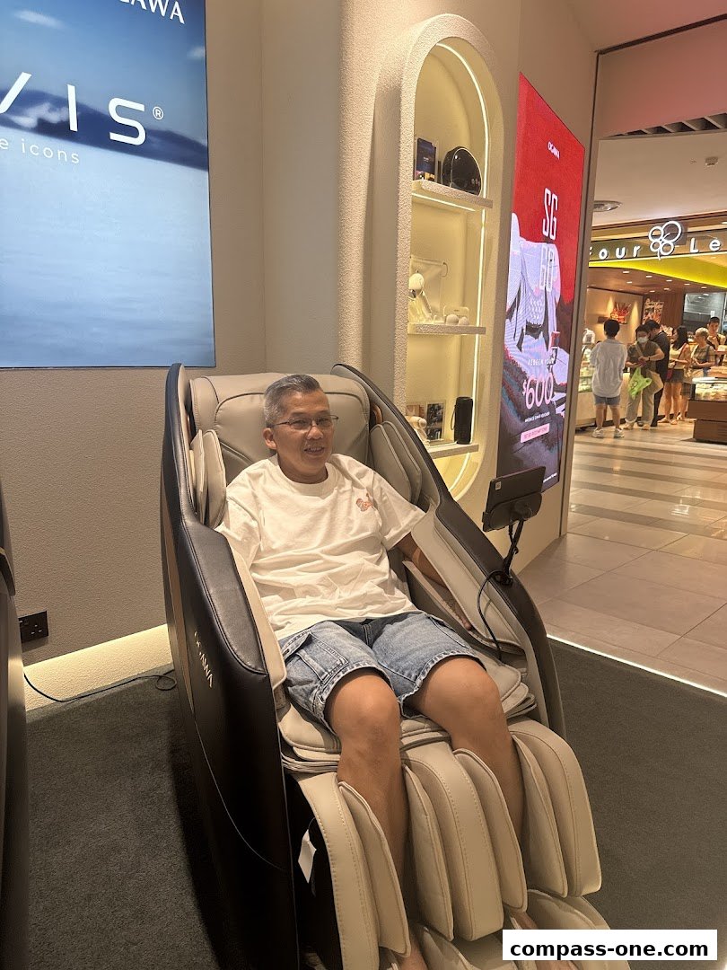 A man sits in a massage chair at the OGAWA store, with other shoppers visible in the background.