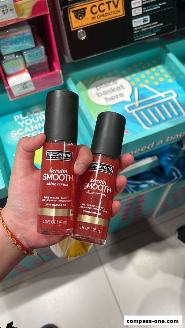 Hands holding two bottles of TRESemmé Keratin Smooth Shine Serum in a retail store.