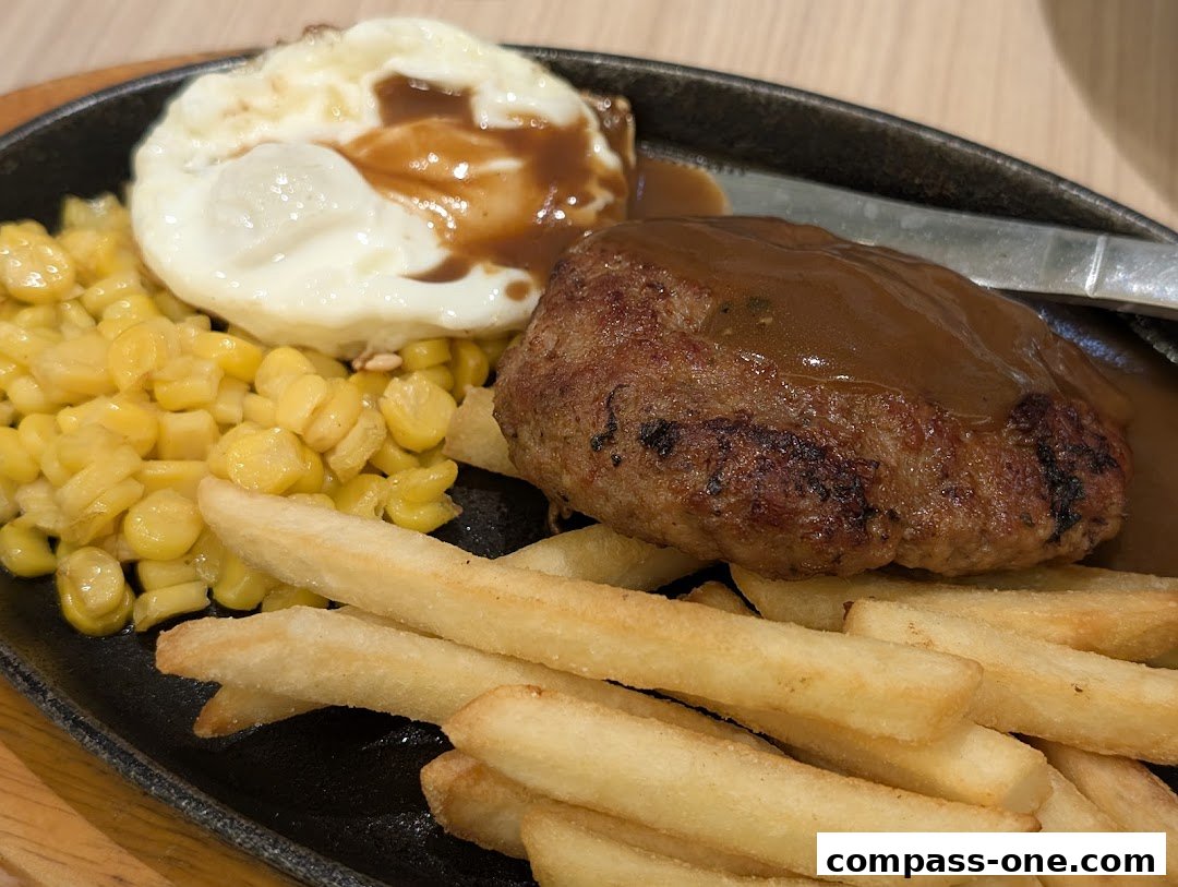 A sizzling hot plate of hamburger steak with a fried egg, corn, and french fries.