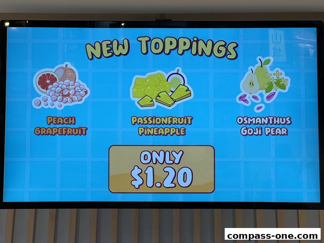 A digital menu board displaying new toppings with fruit illustrations and prices.