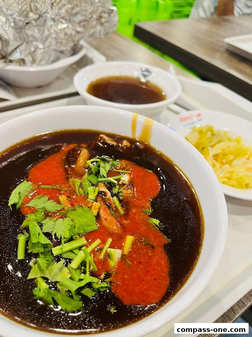 A close-up of a delicious bowl of braised duck with sauce and herbs, served with a side of pickled vegetables.