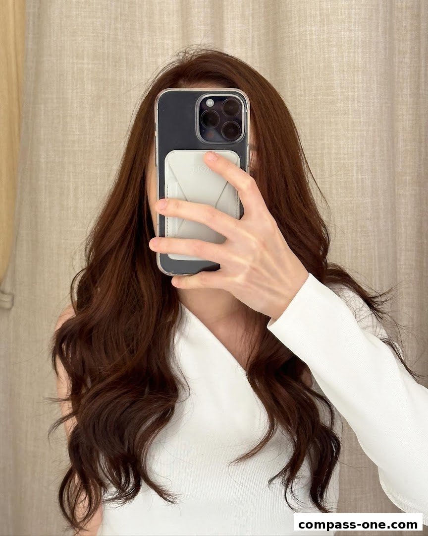 A person with long, wavy brown hair takes a selfie with a smartphone.