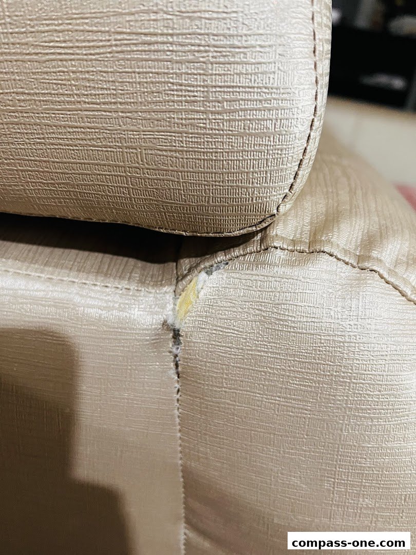 Close-up of a beige textured fabric with a seam and a small tear.